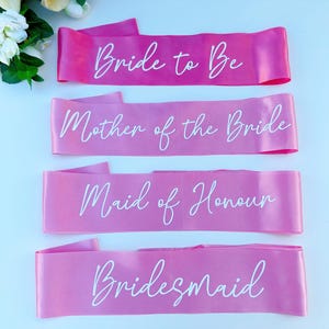 May include: Four pink satin sashes with white script. The sashes read "Bride to Be", "Mother of the Bride", "Maid of Honour", and "Bridesmaid".
