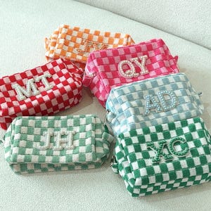 May include: Six checkered fabric cosmetic bags with pearl-embellished initials. The bags are in various colours, including red, pink, green, blue, and orange.