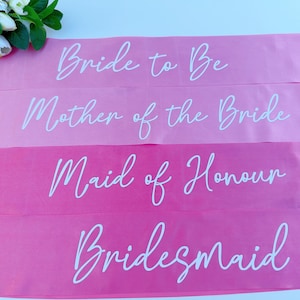 May include: Four pink satin sashes with white text. The sashes read "Bride to Be", "Mother of the Bride", "Maid of Honour", and "Bridesmaid".