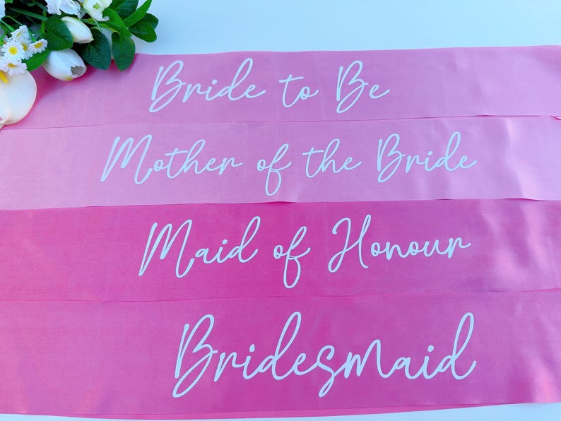 May include: Four pink satin sashes with white text. The sashes read "Bride to Be", "Mother of the Bride", "Maid of Honour", and "Bridesmaid".