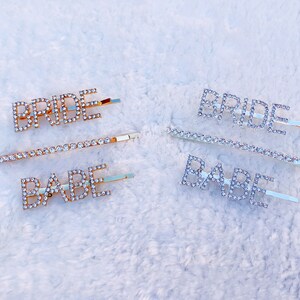 May include: Two sets of hair clips with rhinestone lettering. One set says "BRIDE" and "BABE" in gold. The other set says "BRIDE" in silver.