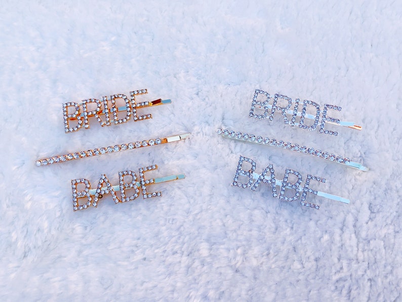 May include: Two sets of hair clips with rhinestone lettering. One set says "BRIDE" and "BABE" in gold. The other set says "BRIDE" in silver.