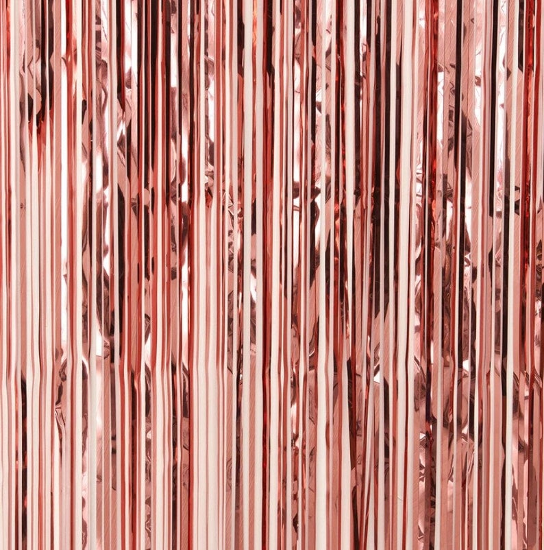 May include: A close-up of a rose gold metallic curtain made of thin strips of foil. The curtain is made of many vertical strips of foil that are overlapping.