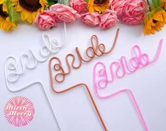 May include: Three plastic straws shaped to spell out the word "bride" in white, brown, and pink.
