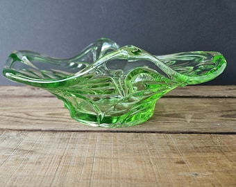 May include: A bright green glass bowl with a wavy rim. The bowl features a textured, geometric pattern and is displayed on a wooden surface. The bowl is approximately 20 cm in diameter.