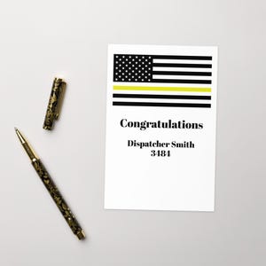 May include: A white card with a black and yellow American flag design, the words "Congratulations" and "Dispatcher Smith 3484". A black and gold pen and pen cap are on the left.