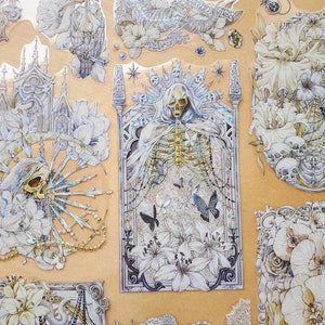 May include: A set of vintage-style stickers featuring a skeleton with wings, flowers, and other gothic imagery. The stickers are printed on clear, glossy paper and have a white background.
