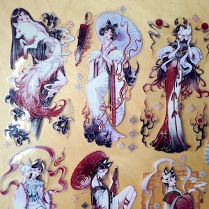 May include: A sheet of stickers featuring anime-style illustrations of women with fox ears and tails. The stickers have a fantasy theme, with characters in elaborate outfits, holding umbrellas, and accompanied by skulls and other mystical elements.