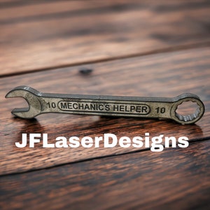 May include: A silver wrench with the text "10 MECHANIC'S HELPER 10" on the handle. The wrench is lying on a wooden surface.