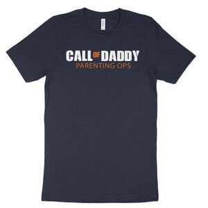 May include: A navy blue t-shirt with the text "CALL OF DADDY PARENTING OPS" in white letters. The word "OF" is in orange.