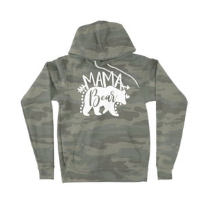 May include: A green camouflage hoodie with a white graphic of a bear and the text "Mama Bear" with an arrow on either side of the text.