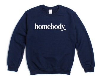 Puede incluir: Una sudadera azul marino con la palabra "homebody" impresa en blanco en la parte delantera. Un pequeño símbolo de corazón está al lado de la palabra.
