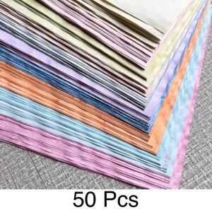 May include: A stack of 50 sheets of colorful paper in various pastel shades, including pink, blue, orange, and yellow. The paper has a textured appearance and is arranged in a diagonal stack. The text "50 Pcs" is at the bottom.