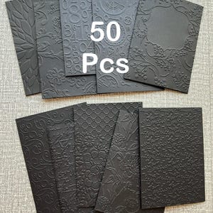 May include: A collection of 50 black embossed cards with various designs, including floral patterns, numbers, and geometric shapes. The cards are arranged in a fan shape, showcasing the different textures and styles.