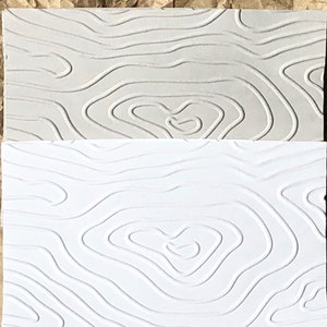 May include: Two textured paper samples, one light gray and one white, with a raised pattern of wavy lines resembling a topographic map.