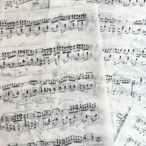 May include: A collection of overlapping translucent sheets of white paper printed with black musical notation. The staff lines, clefs, notes, and dynamic markings are visible through the layered semi-transparent pages, creating a complex pattern.