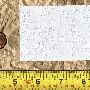 May include: A white textured sheet of paper with a repeating pattern of embossed swirls. The sheet is approximately 2 inches by 3 inches.