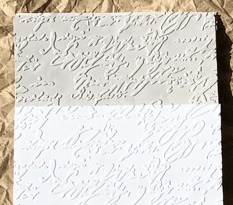 May include: Two sheets of embossed paper with a white and gray pattern. The pattern is a series of abstract swirls and lines.