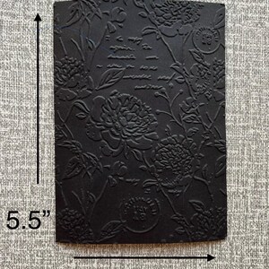 K&ouml;nnte beinhalten: Ein schwarzes, rechteckiges, gepr&auml;gtes Papier mit floralem Design und Schrift. Das Papier misst 14 cm x 10 cm. Das florale Muster umfasst gro&szlig;e, pfingstrosenartige Bl&uuml;ten und Bl&auml;tter. Die Schrift ist teilweise sichtbar.