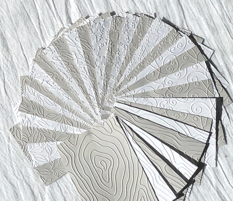 May include: A fan of 20 different embossed paper sheets in various shades of gray. Each sheet has a unique pattern, including swirls, leaves, and lines.