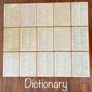 May include: A collection of 12 vintage dictionary pages, each featuring a different letter of the alphabet. The pages are printed on aged paper with a cream background and black text. The pages are arranged in a grid pattern on a wooden surface.
