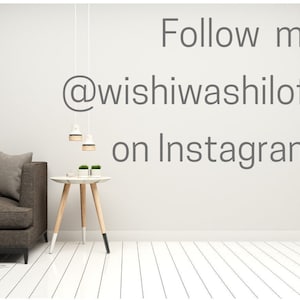 May include: A gray couch with a throw blanket sits in a room with white walls and white wood floors. Two hanging lights are visible above a small wooden table with two potted plants. The text "Follow me @wishiwashiloft on Instagram" is written on the wall.