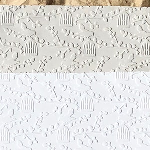 May include: Two sheets of embossed paper with a repeating pattern of birds in cages and branches. The top sheet is a light gray color and the bottom sheet is white.