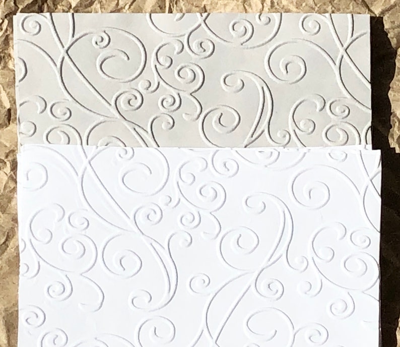 May include: Two sheets of white embossed paper with a swirling pattern. The top sheet is a lighter shade of white.