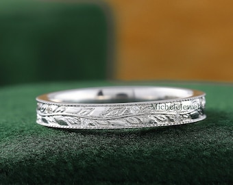 May include: A thin silver band with a delicate floral design engraved around the entire band. The band is sitting on a green velvet surface.