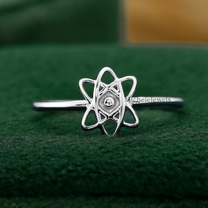 May include: A silver ring with a unique openwork design. The ring features a central element surrounded by a starburst pattern. The ring is set against a green background, highlighting the intricate details of the jewelry.