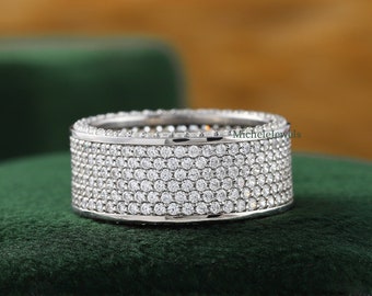 May include: A silver band ring with multiple rows of small, clear cubic zirconia stones. The ring is on a green velvet surface.