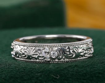 May include: A silver ring with an intricate floral pattern and small, round gemstones. The ring is set against a dark green background, highlighting its detailed design and craftsmanship. The ring's band features a repeating pattern of leaves and flowers.