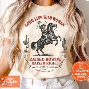 May include: Cream-colored t-shirt with a graphic of a cowgirl on a rearing horse, lasso in hand, and the text "LONG LIVE WILD WOMEN." Below, it reads "RAISED ROWDY, RAISED RIGHT." Cactus illustrations flank the image.