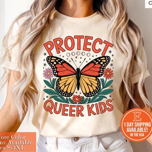 May include: Cream-colored t-shirt featuring a colorful butterfly design with the text "PROTECT QUEER KIDS" in red. The butterfly has orange and yellow wings. Additional text includes "+More Color Options Available Sizes S-3XL" and "1 DAY SHIPPING AVAILABLE! IN THE USA".