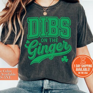 May include: Dark gray t-shirt with the text "DIBS ON THE Ginger" in green, along with a shamrock graphic. The shirt has a vintage look and is available in sizes S-3XL.