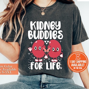May include: A dark grey t-shirt with the text "KIDNEY BUDDIES FOR LIFE" in white. Two cartoon red kidneys with faces are holding hands.