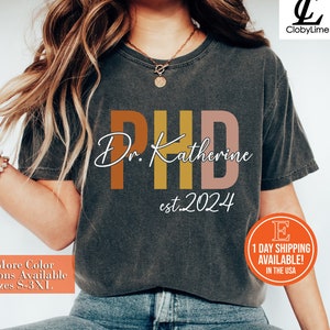 May include: A gray t-shirt with the text "Dr. Katherine PHD est. 2024" in orange, yellow, and pink lettering.