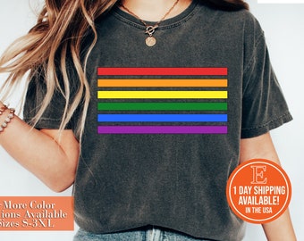 May include: A dark gray t-shirt with a rainbow stripe design. The shirt is available in sizes S-3XL.