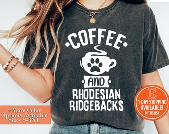 May include: A gray t-shirt with the text "COFFEE. AND RHODESIAN RIDGEBACKS." in white. The text is centered on the shirt and includes a graphic of a coffee cup with a paw print.