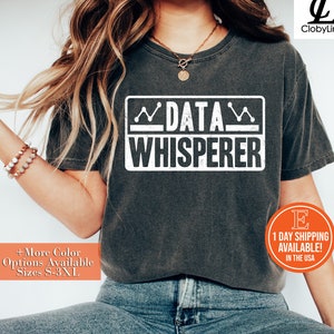 May include: A dark grey t-shirt with a white graphic that says "DATA WHISPERER" in a distressed font. The graphic is surrounded by a white box with a wavy line on top and bottom.