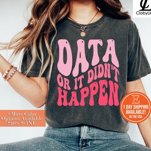 May include: Dark grey t-shirt with the text "DATA OR IT DIDN'T HAPPEN" in pink and hot pink. The shirt has a crew neck and short sleeves. Additional text on the shirt includes "+More Color Options Available Sizes S-3XL".