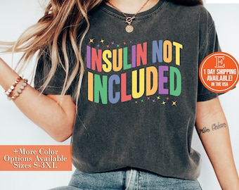 May include: A dark grey t-shirt with the text "INSULIN NOT INCLUDED" in rainbow colors. The text is in a bold, blocky font. The shirt is being worn by a person with long brown hair.