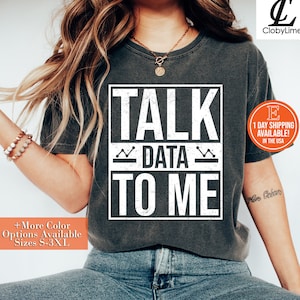 May include: A dark gray t-shirt with the text "TALK DATA TO ME" in white, with a wavy line above and below the word "DATA".