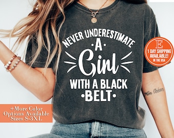 May include: A gray t-shirt with the text "Never underestimate a girl with a black belt." printed in white.