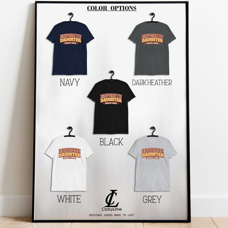Puede incluir: Una exhibici&oacute;n enmarcada de camisetas en varios colores: azul marino, gris oscuro, negro, blanco y gris. Cada camiseta presenta el texto "FAVORITE DAUGHTER SINCE 1999" en un estilo retro. La exhibici&oacute;n incluye el logotipo de la marca.