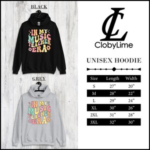 Pode incluir: Hoodie unissex com o texto "In My Music Teacher Era" em uma fonte retr&ocirc; com letras e flores coloridas. O hoodie est&aacute; dispon&iacute;vel em preto e cinza. Um gr&aacute;fico de tamanhos mostra o comprimento e a largura do hoodie em polegadas para os tamanhos S, M, L, XL, 2XL e 3XL.
