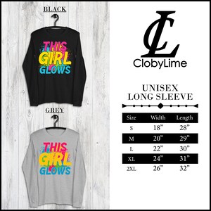 Puede incluir: Camiseta de manga larga unisex con el texto "This Girl Glows" en salpicaduras de pintura de colores. La camiseta est&aacute; disponible en negro y gris. La tabla de tallas muestra las medidas en pulgadas.
