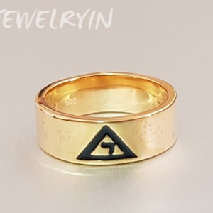 May include: A gold ring with a black triangle and the Hebrew letter "Chai" inside. The ring is a wide band.