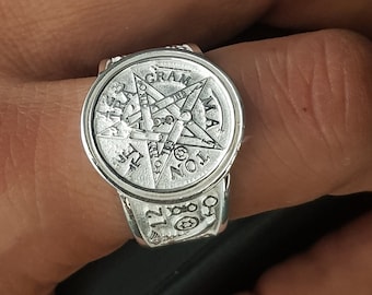 May include: A silver ring with a pentagram design and the words "GRAM, MAT, TON, IST, and  TET" around the outside.