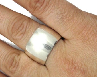 May include: A wide, polished silver ring. The ring has a smooth, rectangular design and is worn on a finger. The ring is a bold statement piece of jewelry.
